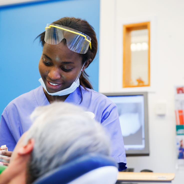 Kvinnlig tandläkare med skyddsglasögon i pannan sitter bredvid en patient.